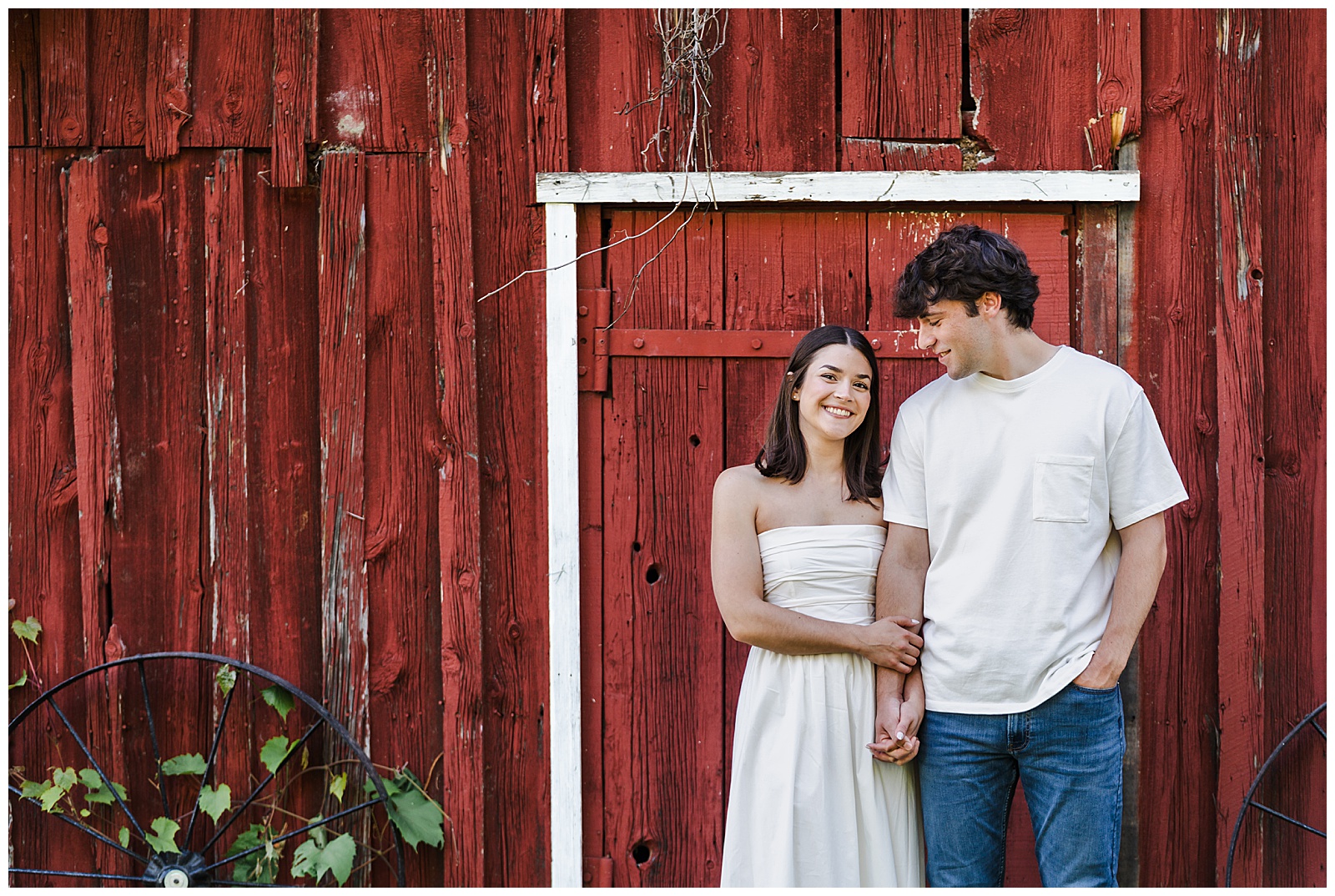 Couple holding hands and smiling in front of a rustic red barn