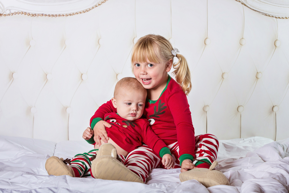 Siblings dressed for Christmas sitting on a bed