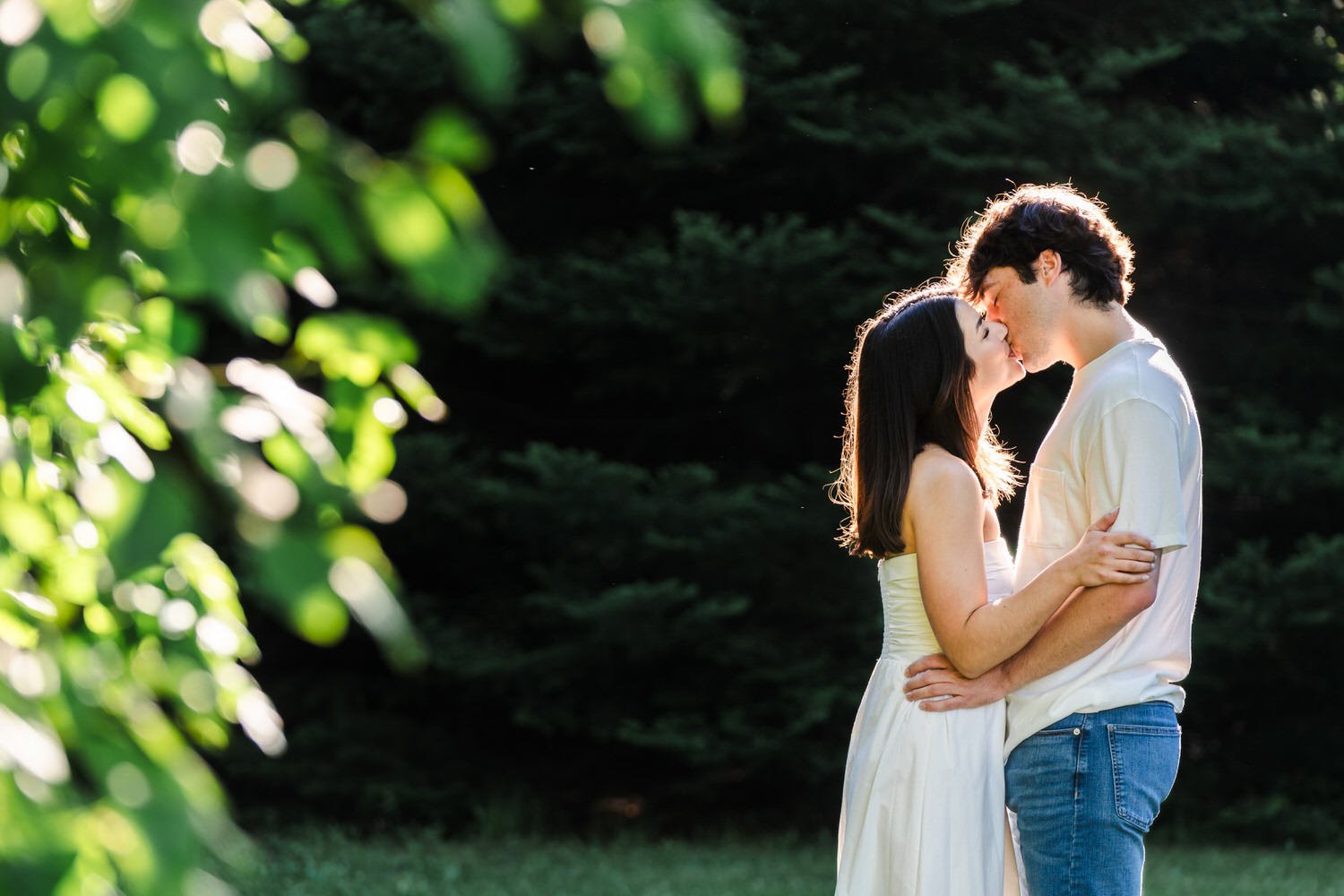 Couple kissing and embracing outdoors in warm natural light surrounded by greenery